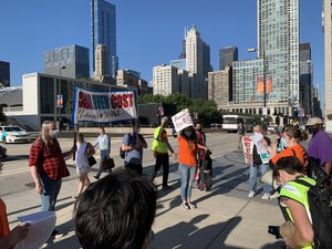 People protesting in a open space area with city build behind