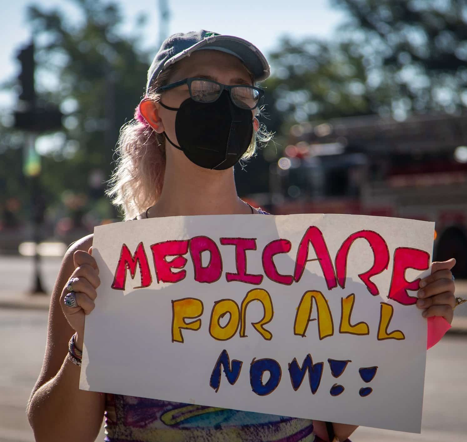 Person holding medicare for all now sign