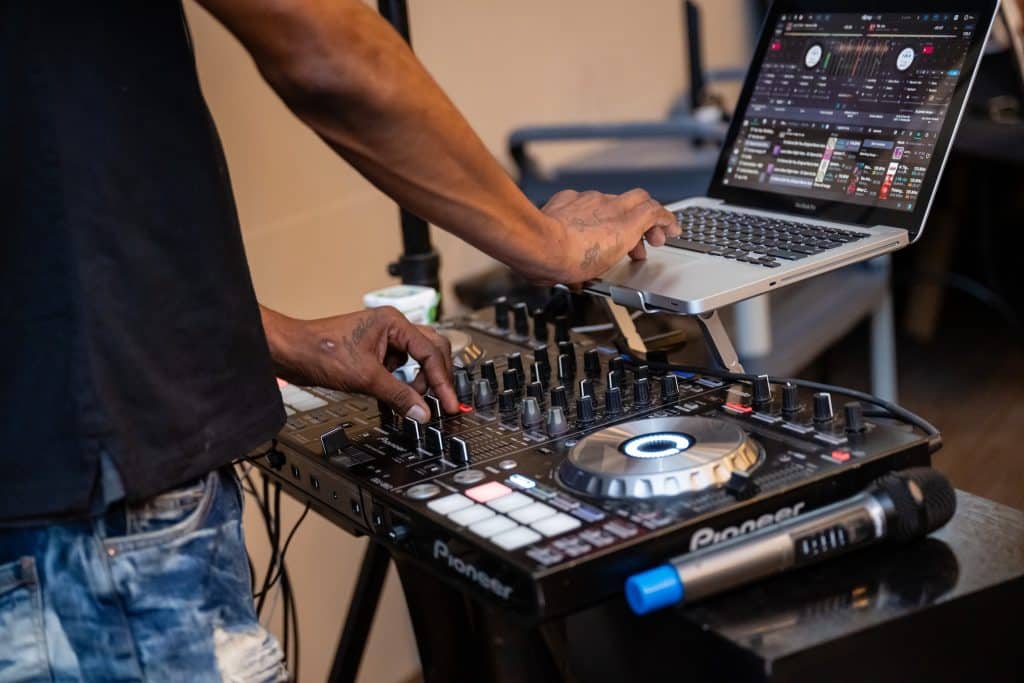This is a DJ. Hands control buttons on a laptop and a mixing board.