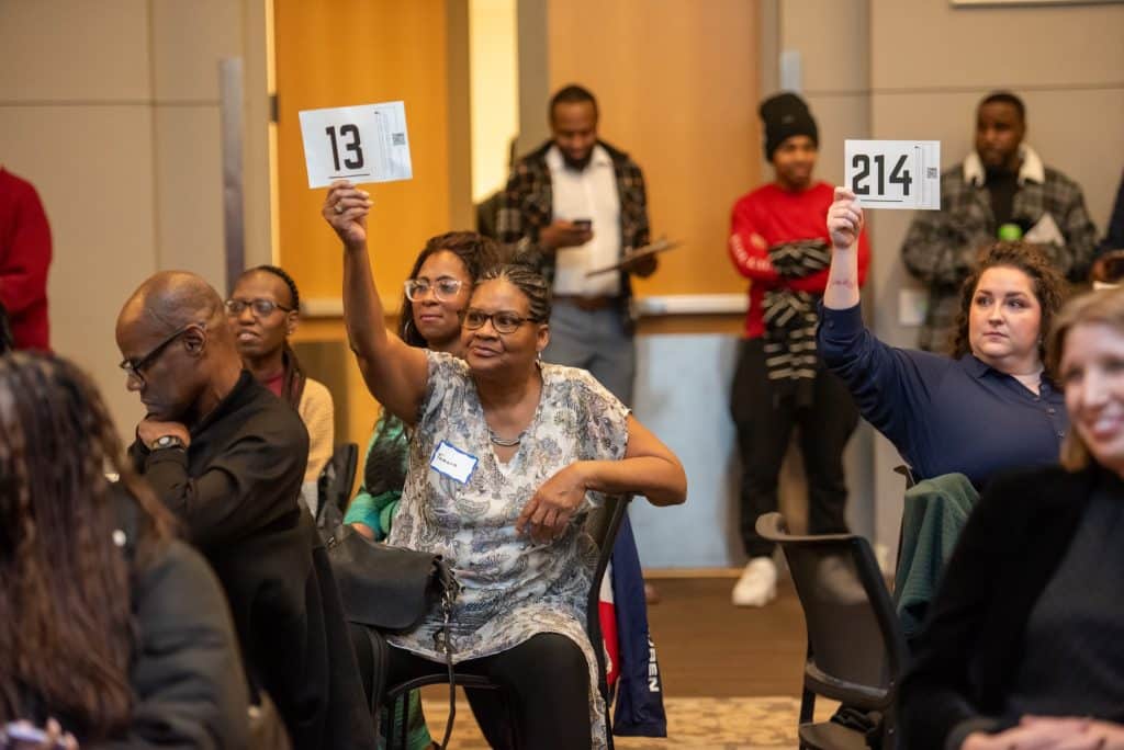 Several people watching the paddle raise, two of them are holding up cards with numbers