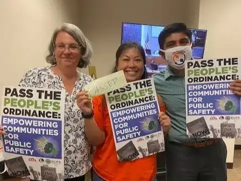 Three People Holding Up Paper Pass The People Ordinance